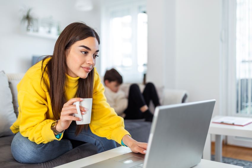 mujer joven mirando la pantalla del portátil con una taza de café en la mano_lead generation