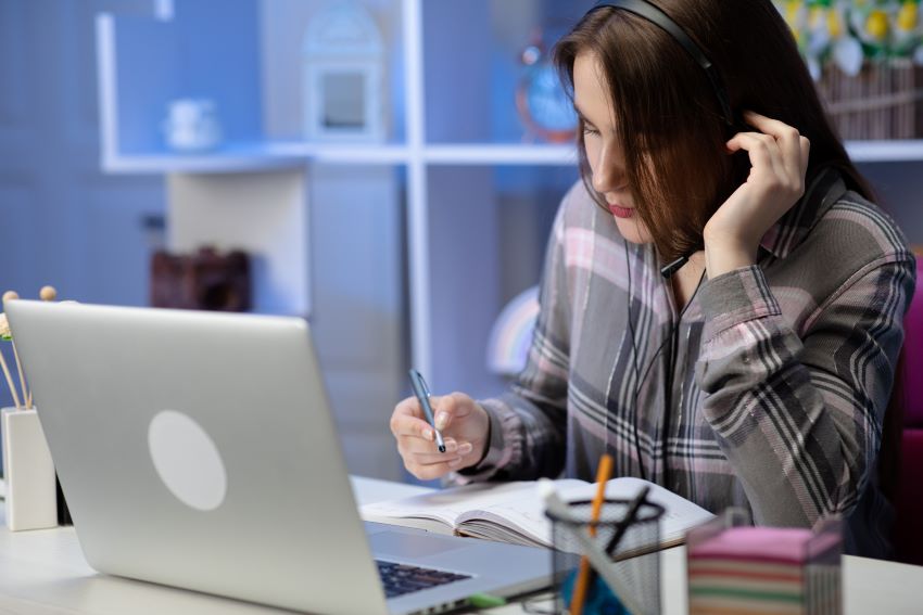 cómo promocionar cursos online_mujer con auriculares escribiendo frente a un portátil